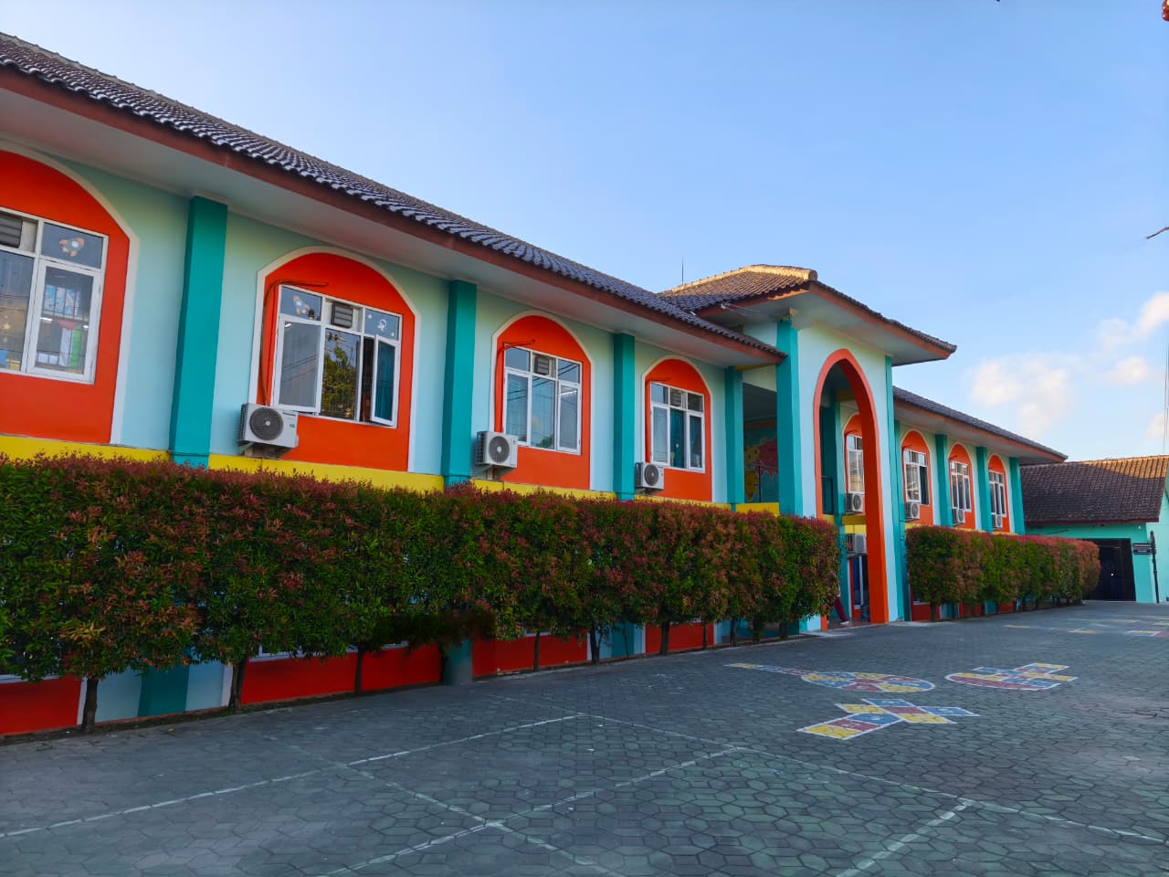 Modern eco-friendly primary school campus with lush greenery, wooden architecture, and children playing in soft afternoon sunlight